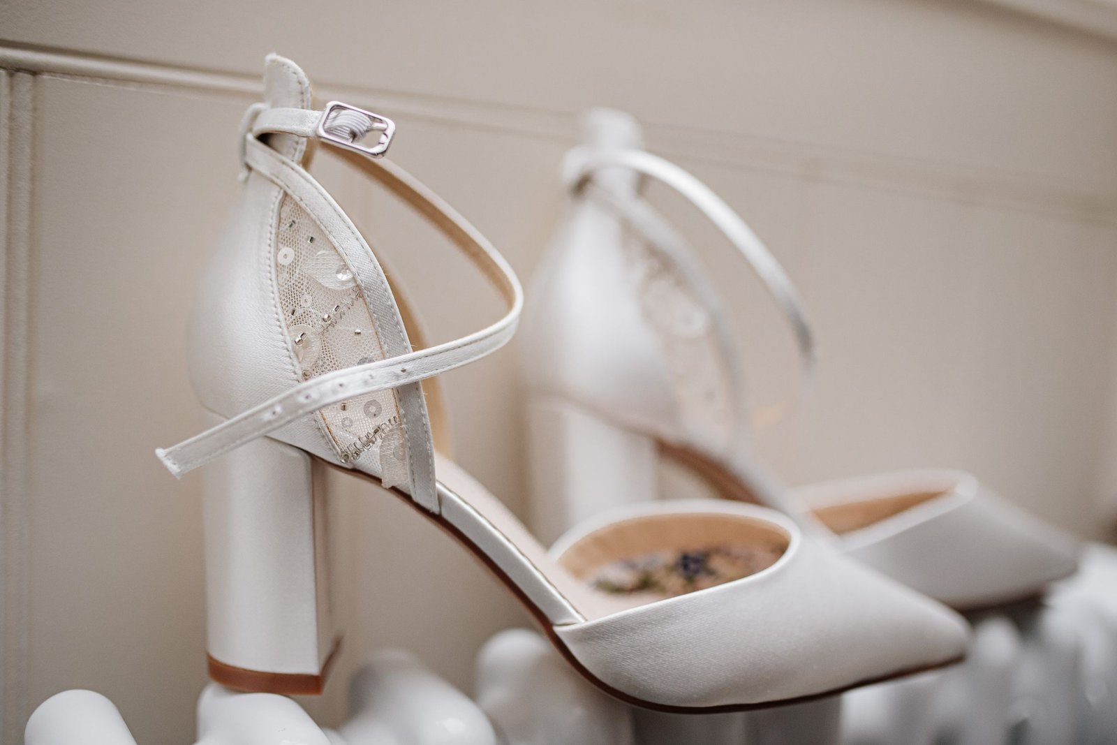Escarpin de mariée en cuir ivoire posé sur un tapis de cérémonie, à côté d'un bouquet de fleurs blanches